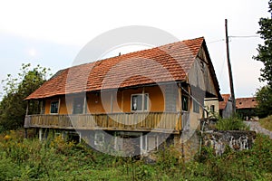 Abandoned stone and wooden family house with front porch surrounded with overgrown forest vegetation next to tall wooden utility
