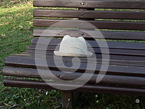 Abandoned straw hat left on a wooden bench in park.