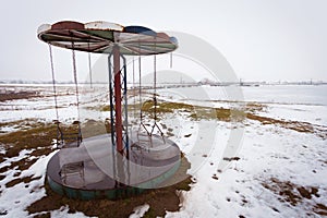 Abandoned swing carousel with broken chains in winter