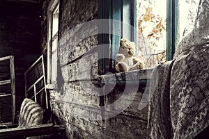 An abandoned teddy bear with reliable looks out the window of an abandoned house