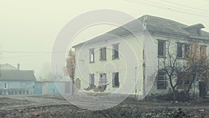 An abandoned two-story wooden house by the road on a foggy day