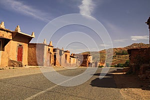 Abandoned village of clay houses along empty road in Atlas mountains, Morocco