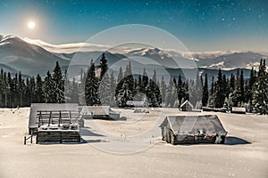 Abandoned village, wooden cabins in winter Carpathian mountains under moonlight