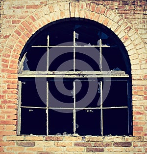 Abandoned warehouse facade detail with grungy broken window and broken glasses on a red brick wall