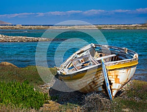 abandoned wooden fish boat at the shore. The boat is destroyed and rusty an completely useless with the sea and the blue sky at