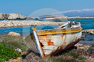 abandoned wooden fish boat at the shore. The boat is destroyed and rusty an completely useless with the sea and the blue sky at