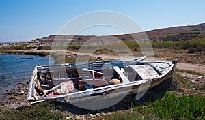 abandoned wooden fish boat at the shore. The boat is destroyed and rusty an completely useless with the sea and the blue sky at