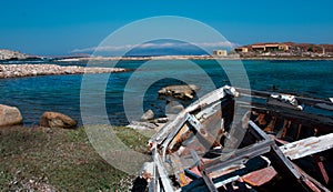 abandoned wooden fish boat at the shore. The boat is destroyed and rusty an completely useless with the sea and the blue sky at