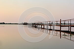 Abandoned wooden long bridge and its reflection over still water on sunrise