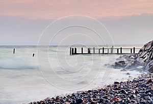 Abandoned wooden wharf in sea within sunrise.Gentle blue pink color of sky, blur waves