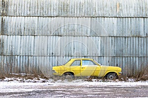 An abandoned yellow car against a wall