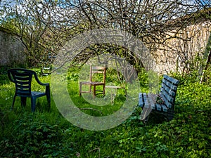 Abandonned chairs and a bench in an overgrown lawn closed with limestone walls