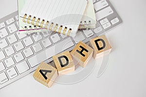 Abbreviation of ADHD on wood cube block with computer keyboard and note book on white table. Attention Deficit Hyperactivity