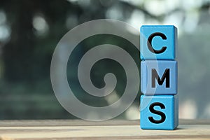 Abbreviation CMS of blue cubes on wooden table against blurred background, space for text. Content management system