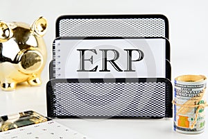Abbreviation ERP - Enterprise Resource Planning on a white notepad with money and a piggy bank in the background out of focus