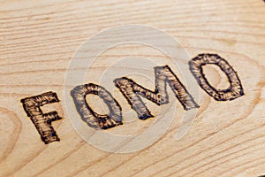 Abbreviation FOMO - fear of missing out - burnt by hand on flat wooden surface. Diagonal view with selective focus