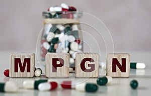 Abbreviation MPGN text on wooden cubes on a light background with a jar of pills