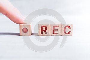 The Abbreviation REC Formed By Wooden Blocks And Arranged By A Male Finger On A White Table