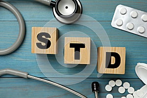 Abbreviation STD made with cubes, pills and stethoscope on light blue wooden table, flat lay