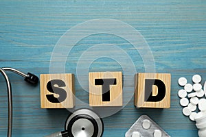 Abbreviation STD made with cubes, pills and stethoscope on light blue wooden table, flat lay. Space for text