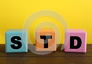 Abbreviation STD made with cubes on wooden table against yellow background