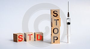 The abbreviation STD STOP formed by wooden blocks on a white table. Next to it is a syringe - a threat to life, a medical concept