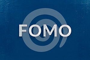 The abbreviation word fomo - fear of missing out - laid with silver letters on classic blue color flat surface