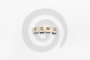 Abbreviation word FOMO from wooden blocks on white background. FOMO means Fear Of Missing Out, non-stop internet surfing. Concept