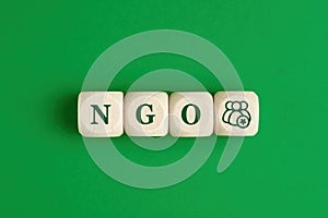 The abbreviation word NGO nongovernmental organization written on wooden cubes with people icon on green background