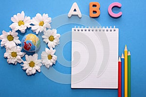 ABC-the first letters of the English alphabet on a blue background next to the small globe and white chrysanthemums. Notebook and