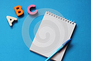 ABC-the first letters of the English alphabet on a blue background. Notebook and pen. Empty space for text. Learn foreign