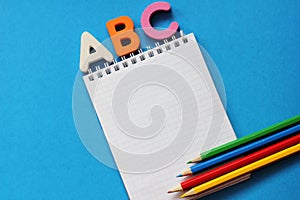 ABC-the first letters of the English alphabet on a blue background. Notebook and pencils of different colors . Empty space for