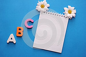 ABC-the first letters of the English alphabet on a blue background. Notebook and white chrysanthemum . Empty space for text. Learn