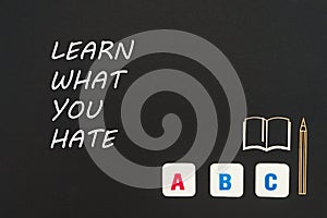 ABC letters and chipboard miniature on blackboard with text learn what you hate