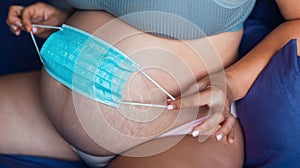 abdomen of a pregnant girl with a medical, disposable, blue mask near her abdomen Belly pregnant close-up
