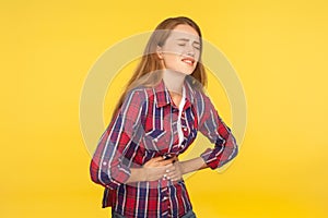 Abdominal pain. Portrait of unhealthy ginger girl in shirt clasping belly and suffering stomachache, indigestion symptoms photo