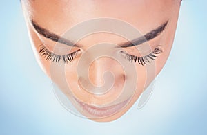 Above, beauty and woman face with closeup, studio and natural for skincare on blue background. Dermatology, mascara and