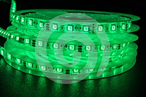 From above bobbins with three roll of glowing LED strip lighting,colour green, placed on table in dim room