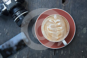 Above cup of hot latte art coffee with smart phone and camera.