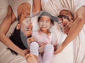 Above, family and child happy on bed smile, laugh and bonding on weekend. Mom, dad and parents with kid in pajamas