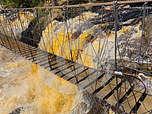 Above the fountain with yellow-brown water and protruding stones there is a rope wooden ladder