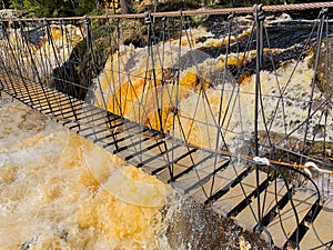 Above the fountain with yellow-brown water and protruding stones there is a rope wooden ladder