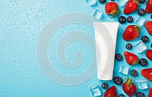Above photo of berries strawberries blueberries transparent cubes ice water drops and white tube of cream isolated on the blue