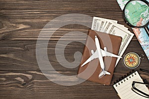 Above photo of brown passport wit money dollars cash inside plane map magnifier compass notepad and glasses isolated on the wooden