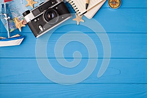 Above photo of camera map starfish ship notepad pen and compass isolated on the blue wooden background with copyspace