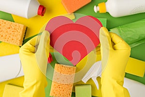 Above photo of hands in yellow gloves with pink card as heart isolated on the background of equipment for cleaning