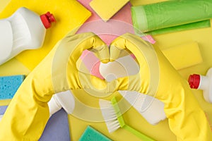 Above pov photo of equipment for cleaning and hands in yellow gloves with gesture as heart isolated on the yellow background