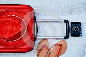 From above red suitcase beside flip-flop and retro camera on light background. Travel blogging or woman blogger or summer vacation