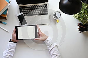 Above shot businessman holding a computer tablet with white blank screen in hands at the modern white table.