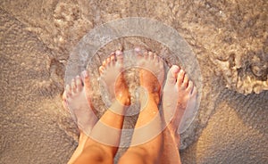 Above shot of the feet of a caucasian couple in the ocean while standing on the sand at the beach. Romantic people